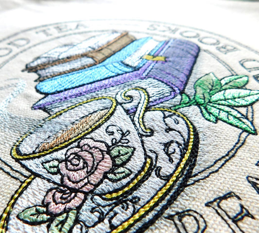 Embroidered design of a teacup with flowers and books on a circular background for a 100% cotton tote bag