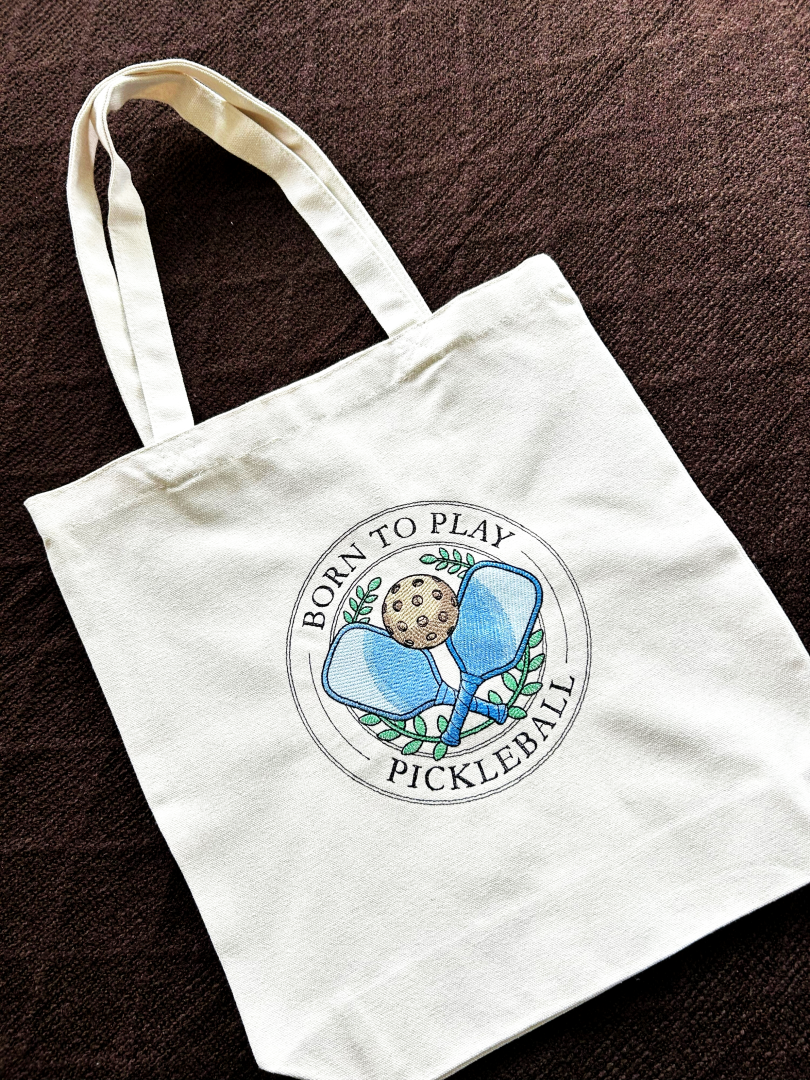 White embroidered tote bag in Calgary with pickleball design and text on a brown surface