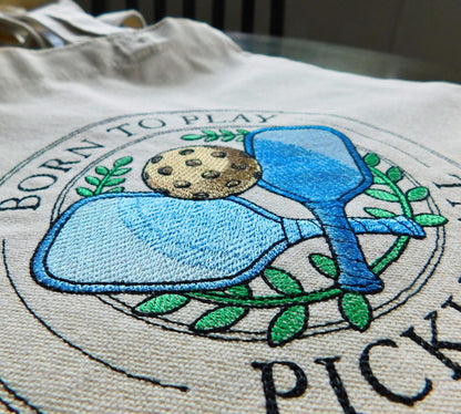 Embroidered design on a tote bag with text and blue and green elements.