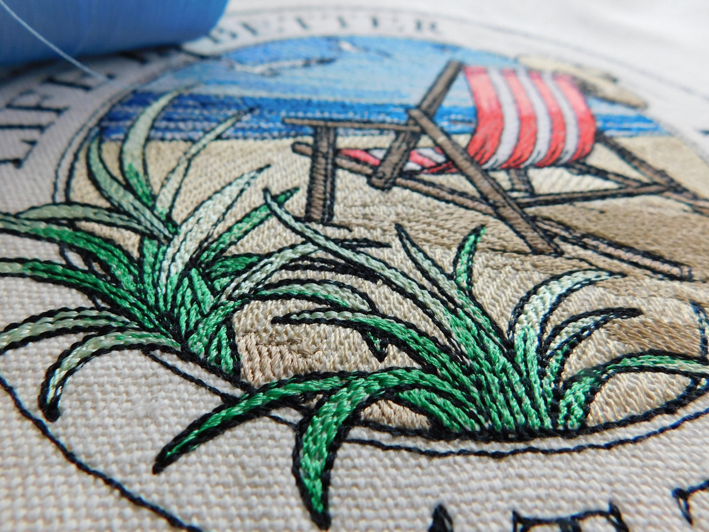 Embroidery of a beach scene with grass, lounge chairs, and an red striped beach chair tote bag.
